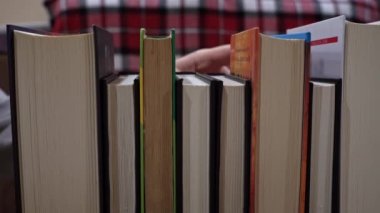 Young girl chooses a book on a shelf with books. Library bookshelves background stack of books. The pages of the book are turning. Reading scientific literature surrounded by books.