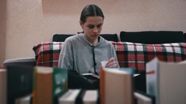 Young girl reads a book on the background of a shelf with books. Library bookshelves background stack of books. The pages of the book are turning. Reading scientific literature surrounded by books.