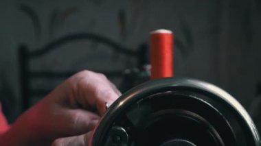 Woman winds a thread for sewing on a typewriter close-up. An elderly woman in glasses sews on an old sewing machine. A seamstress makes a machine-made even seam on a red fabric.