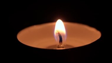 Paraffin candle burns in the dark with a yellow flame. A large fire in a wax candle burns yellow. There is no light in the house, heat from a candle. Poverty, war, a moment of silence.
