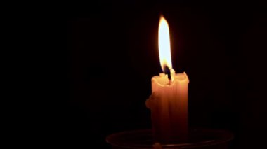 Paraffin candle burns in the dark with a yellow flame. A large fire in a wax candle burns yellow. There is no light in the house, heat from a candle. Poverty, war, a moment of silence.