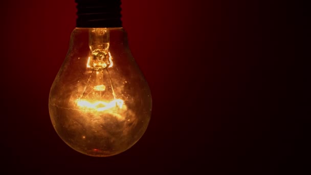 電球は暗闇の中で赤い背景に出て行きます タングステン球をゆっくりとオフにします 点滅するヴィンテージ電球のフィラメント エネルギー イノベーションの概念 — ストック動画
