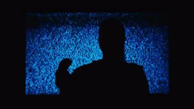 Silhouette of a girl watching TV with noises, shot from the back. Watching TV is a static glitch. Silhouette of a girl watching TV with static noise. Shot behind the shoulders of the model.