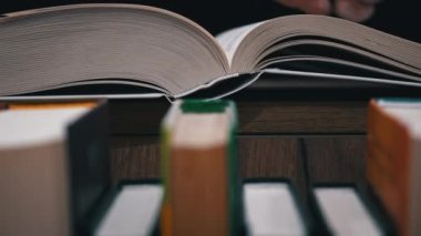 Young girl reads a book on the background of a shelf with books. Library bookshelves background stack of books. The pages of the book are turning. Reading scientific literature surrounded by books.