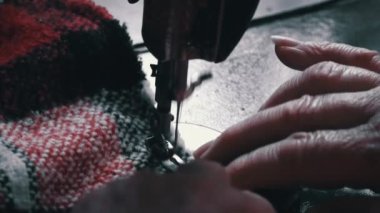 Aged woman sews on an old sewing machine. Needle and foot of sewing machine penetrates fabric with high magnification and super slow motion. Seamstress makes a machine-made even seam on red fabric.