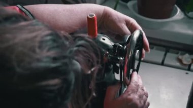 Woman winds a thread for sewing on a typewriter close-up. An elderly woman in glasses sews on an old sewing machine. A seamstress makes a machine-made even seam on a red fabric.