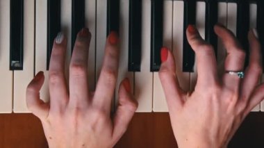 Female hands with fingers play the piano keyboard close-up top view. The piano keys are black and white. Musical instrument, spiritual education, calm music.