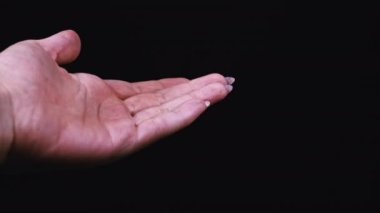 Kadın eline siyah arka plandaki bir kavanozdan beyaz haplar döküyor. Kız elinde tuttuğu kapsül dağını inceliyor. Evinde bir kadın duruyor, evinde ilaçlarla.