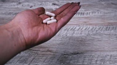 Woman pours white pills into her hand from a jar. The girl examines the mountain of capsules that she has in her hand. A woman stands in her house, apartment with medicine in her hand.
