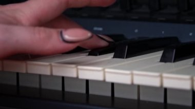 Female hands with fingers play the piano keyboard close-up side view. The piano keys are black and white. Musical instrument, spiritual education, calm music.