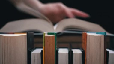 Young girl reads a book on the background of a shelf with books. Library bookshelves background stack of books. The pages of the book are turning. Reading scientific literature surrounded by books.