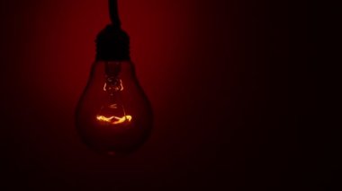 Light bulb lights up and goes out on a red background in the dark. Slow turning on and off of a tungsten light bulb. Filament of a blinking vintage light bulb. Energy, electricity, light, life.