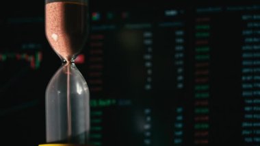 Hourglass is falling on background of a crypto exchange close-up. Time is money. With every minute, cryptocurrency rises or falls. Eth and btc quotes on stock exchange. Stock market chart.