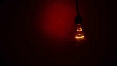 Karanlıkta kırmızı arka planda ampul tökezler. Tungsten ampulü yavaş yavaş açıp kapanıyor. Yanıp sönen eski bir ampulün filamanı. Enerji, elektrik, ışık, yaşam.