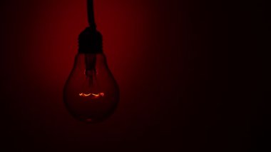 Light bulb lights up on a red background in the dark. Slow turning on of the tungsten bulb. Filament of a blinking vintage light bulb. Energy, electricity, light, life. Innovation concept.