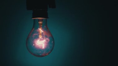 Light bulb lights up and goes out on a blue background in the dark. Slow turning on and off of a tungsten light bulb. Filament of a blinking vintage light bulb. Energy, electricity, light, life.