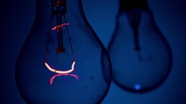 Light bulb flashes on a blue background in the dark. Slow turning on and off of a tungsten light bulb. Filament of a blinking vintage light bulb. Energy, electricity, light, life.