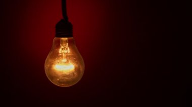 Light bulb goes out on a red background in the dark. Slow turning off of the tungsten bulb. Filament of a blinking vintage light bulb. Energy, electricity, light, life. Innovation concept.