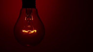 Light bulb lights up and goes out on a red background in the dark. Slow turning on and off of a tungsten light bulb. Filament of a blinking vintage light bulb. Energy, electricity, light, life.