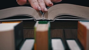 Young girl reads a book on the background of a shelf with books. Library bookshelves background stack of books. The pages of the book are turning. Reading scientific literature surrounded by books.
