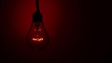 Light bulb lights up and goes out on a red background in the dark. Slow turning on and off of a tungsten light bulb. Filament of a blinking vintage light bulb. Energy, electricity, light, life.