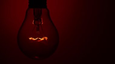Light bulb lights up and goes out on a red background in the dark. Slow turning on and off of a tungsten light bulb. Filament of a blinking vintage light bulb. Energy, electricity, light, life.