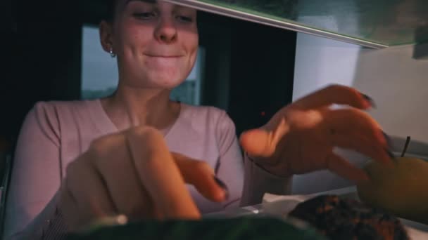 Piękna Wesoła Młoda Kobieta Otwiera Lodówkę Jedzeniem Gryzie Babeczkę Widok — Wideo stockowe