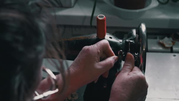 女性はタイプライターのクローズアップで縫製するための糸を巻きます 眼鏡をかけた年配の女性が古いミシンで縫う 縫い目は赤い生地の上に機械製の縫い代を作る — ストック動画