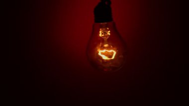 Light bulb staggers on a red background in the dark. Slow turning on and off of a tungsten light bulb. Filament of a blinking vintage light bulb. Energy, electricity, light, life.
