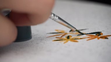 Womans hand draws a picture by numbers. A hand with a manicure paints empty cells by numbers. The girl holds a brush for drawing and draws a picture with acrylic paints.