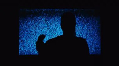 Silhouette of a girl watching TV with noises, shot from the back. Watching TV is a static glitch. Silhouette of a girl watching TV with static noise. Shot behind the shoulders of the model.