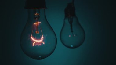Light bulb flashes on a blue background in the dark. Slow turning on and off of a tungsten light bulb. Filament of a blinking vintage light bulb. Energy, electricity, light, life.