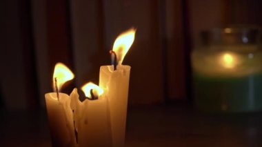 Candles burn in dark against background of a shelf with old books. Atmosphere of old library with yellow candles. Night reading of an old book in low light. Library at night, reading old literature.