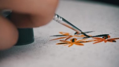 Womans hand draws a picture by numbers. A hand with a manicure paints empty cells by numbers. The girl holds a brush for drawing and draws a picture with acrylic paints.