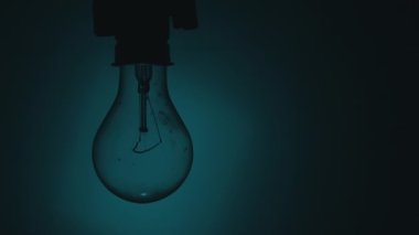 Light bulb flashes on a blue background in the dark. Slow turning on and off of a tungsten light bulb. Filament of a blinking vintage light bulb. Energy, electricity, light, life.