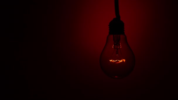 灯泡亮起 在黑暗中在红色的背景上熄灭 慢慢地打开和关闭钨灯灯泡 闪烁的老式灯泡的灯丝 — 图库视频影像