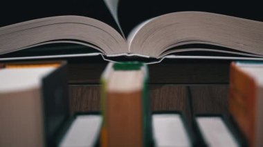 Young girl reads a book on the background of a shelf with books. Library bookshelves background stack of books. The pages of the book are turning. Reading scientific literature surrounded by books.