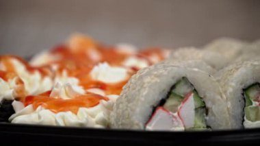 Sushi roll is spinning in a black container close-up. Japanese cuisine sushi in a restaurant. Sushi roll with salmon and vegetables. Japan restaurant menu. Side view.