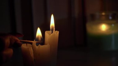 Womans hand lights candles in dark against background of books. Atmosphere of the old library with yellow candles. Night reading of an old book in low light. Library at night, reading old literature.
