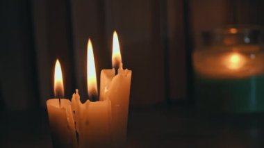 Candles burn in dark against background of a shelf with old books. Atmosphere of old library with yellow candles. Night reading of an old book in low light. Library at night, reading old literature.