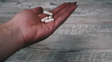 Woman pours white pills into her hand from a jar. The girl examines the mountain of capsules that she has in her hand. A woman stands in her house, apartment with medicine in her hand.