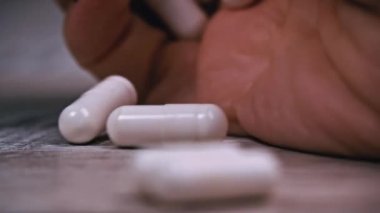 Woman pours white pills into her hand from a jar. The girl examines the mountain of capsules that she has in her hand. A woman stands in her house, apartment with medicine in her hand.