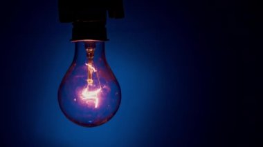 Light bulb lights up and goes out on a blue background in the dark. Slow turning on and off of a tungsten light bulb. Filament of a blinking vintage light bulb. Energy, electricity, light, life.