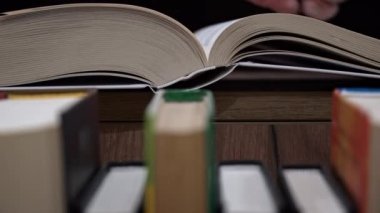 Young girl reads a book on the background of a shelf with books. Library bookshelves background stack of books. The pages of the book are turning. Reading scientific literature surrounded by books.