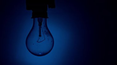 Light bulb flashes on a blue background in the dark. Slow turning on and off of a tungsten light bulb. Filament of a blinking vintage light bulb. Energy, electricity, light, life.