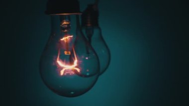 Karanlıkta mavi bir arkaplanda ampul yanıp sönüyor. Tungsten ampulü yavaş yavaş açıp kapanıyor. Yanıp sönen eski bir ampulün filamanı. Enerji, elektrik, ışık, yaşam.