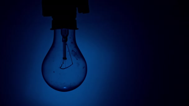 灯泡在黑暗中闪烁着蓝色背景的光芒 慢慢地打开和关闭钨灯灯泡 闪烁的老式灯泡的灯丝 — 图库视频影像
