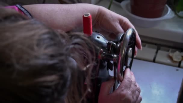女性はタイプライターのクローズアップで縫製するための糸を巻きます 眼鏡をかけた年配の女性が古いミシンで縫う 縫い目は赤い生地の上に機械製の縫い代を作る — ストック動画