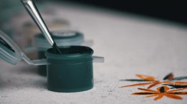 Womans hand draws a picture by numbers. A hand with a manicure paints empty cells by numbers. The girl holds a brush for drawing and draws a picture with acrylic paints.