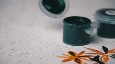 Acrylic paints of different colors stand on the canvas ready to be painted. A hand with a manicure paints empty cells by numbers. Paint brush and draws a picture with acrylic paints.